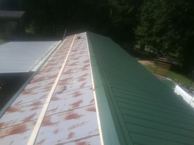 Old rusted panels beside newly installed green metal roofing — Wind Damage Roof Repair by Roofing Brothers in Gainesville