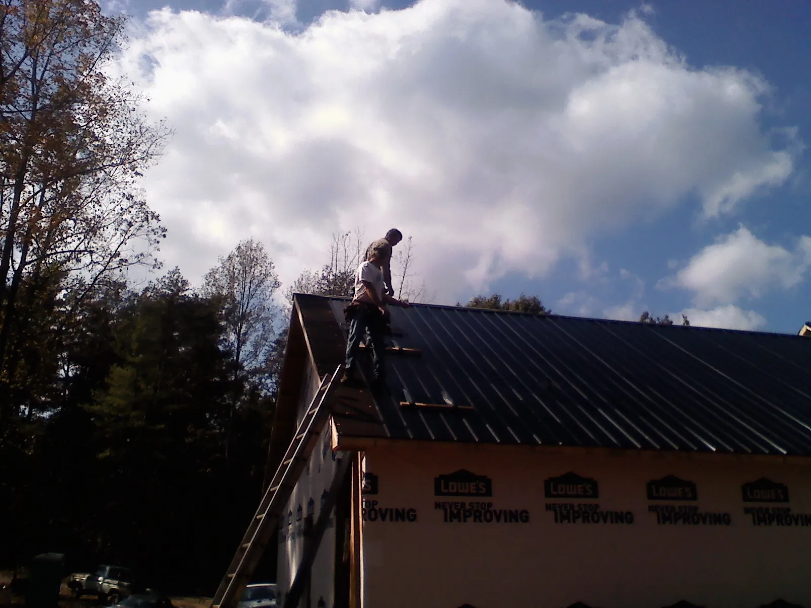 Roofer fastening dark metal panels high against a cloudy sky, from a Roof Inspection job in Gainesville