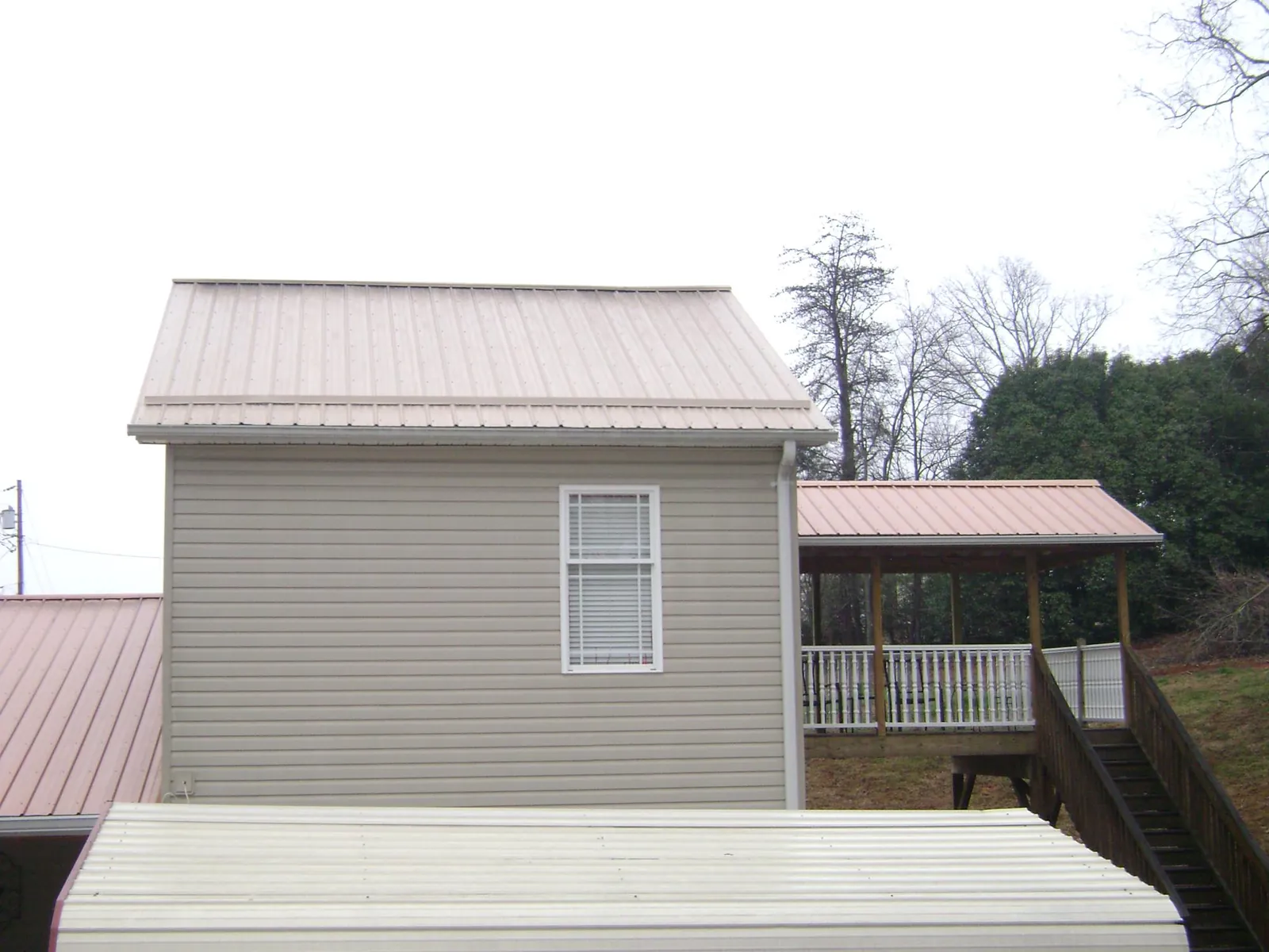 Tan metal roofs on a two story addition and attached porch, from a Roof Replacement job in Gainesville